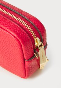 Red leather zippered accessory pouch with a textured finish and gold hardware. Features a prominent zipper and branding detail.
