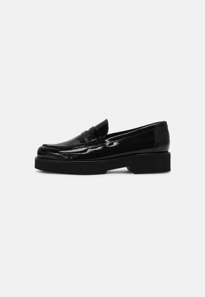 Mocassins en cuir verni noir avec un bout arrondi et une bande texturée sur le devant, reposant sur une semelle plateforme noire épaisse.