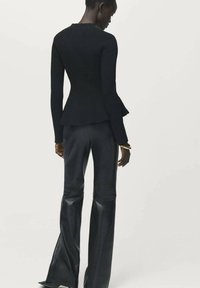 Top lungo a maniche lunghe nero a coste con orlo a peplum fluttuante, abbinato a pantaloni in pelle neri attillati. Texture liscia, design semplice e silhouette elegante.