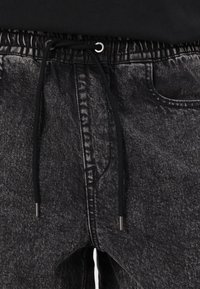Black denim joggers with an elastic waistband, adjustable drawstring, and side pockets. Features a textured finish and silver hardware accents.