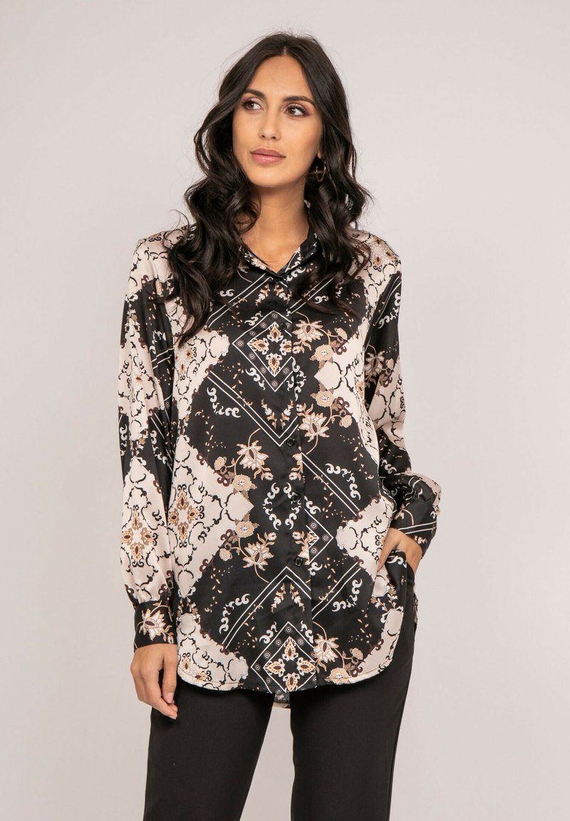 Blouse à manches longues noire et crème, ornée de motifs floraux et géométriques, avec un devant à boutons et un col montant. Texture satin lisse.