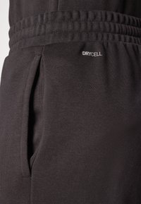 Schwarze Sporttights aus strukturiertem Stoff verfügen über einen elastischen Bund, Seitentaschen und ein „DRYCELL“-Label in der Nähe der Tasche.