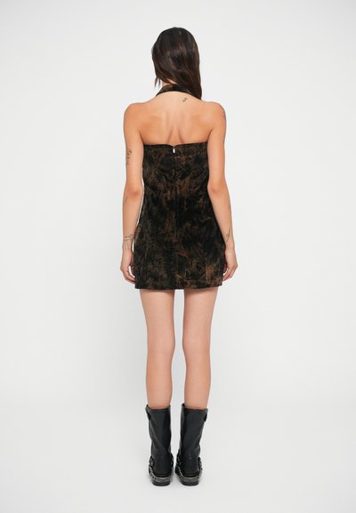 Καφέ μίνι φόρεμα από βελούδο με ελαστική ύφανση, με λαιμόκοψη halter, εφαρμοστή σιλουέτα, κλείσιμο με φερμουάρ στην πλάτη και υφή υφάσματος. Συνδυασμένο με μαύρες μπότες μέχρι το γόνατο.