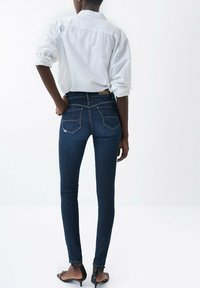 Mörkblå skinny jeans med hög midja, med två bakfickor och sömnadsdetaljer. Matchas med en vit knäppskjorta.