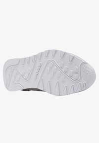 Svart skosula med en vit gummiyttersula som har texturerade greppmönster och en Reebok-logotyp. Designen inkluderar upphöjda cirkulära och vinklade detaljer.