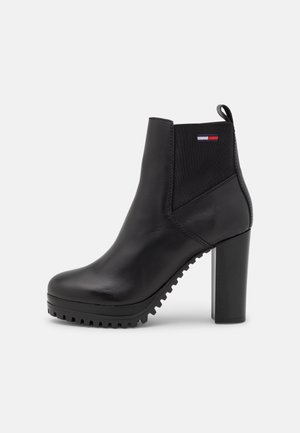 Bottine noire en cuir avec talon bloc, panneau latéral élastique, languette, semelle robuste, et petit logo drapeau rouge, blanc et bleu sur le côté.