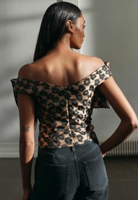 Lāču raksta blūze ar plecus atklājošu dizainu, izgatavota no zīda auduma, ar pieguļošu siluetu un aizmugures rāvējslēdzēju. Kombinēta ar augsto vidukli melniem džinsiem.