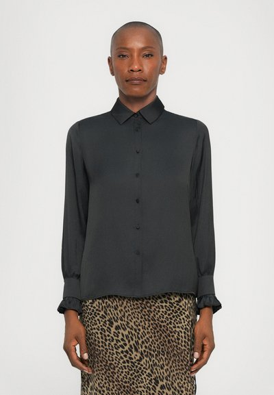 Chemise noire à boutons avec manches longues, tissu doux, et poignets à volants, associée à une jupe imprimée léopard aux différentes nuances de brun.