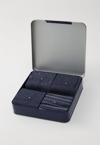 Scatola di latta blu navale contenente quattro paia di calze: due blu scuro uni, una con logo rosso e bianco, una a righe grigie e blu. Materiale in cotone.