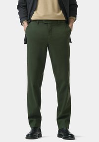 Green cotton trousers with a straight leg design, featuring pockets and a subtle texture. Paired with black footwear for contrast.