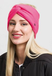 Bandă de cap din fleece roz aprins, cu un design împletit, având un mic accent cu logo. Textura moale completează aspectul cald și confortabil.