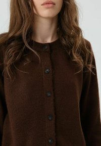 Brauner Strickcardigan mit rundem Ausschnitt, Knopfverschluss mit schwarzen Knöpfen und weicher Textur. Einfaches, klassisches Design.