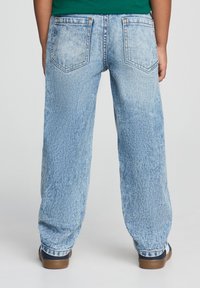 Jeans in denim azzurro chiaro con vestibilità comoda, dotati di due tasche posteriori e una leggera scoloritura. Mostrati da dietro, abbinati a scarpe marroni.