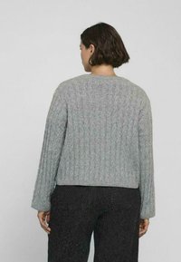 Maglione grigio a coste con maniche lunghe, texture lavorata a maglia e design cropped. Presenta un collo rotondo e una finitura pulita sui bordi.