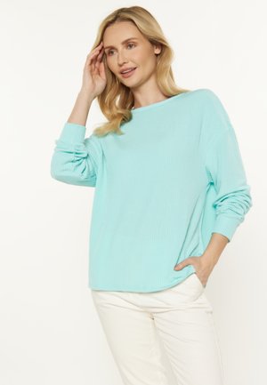Maglione a coste di un blu chiaro con una vestibilità rilassata, scollo ampio e maniche arrotolate, abbinato a pantaloni bianchi. Design semplice e dalla texture. 