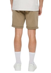 Khakifarbene Baumwollshorts mit umgeschlagenem Saum, kombiniert mit weißen Kniesocken und Sneakers. Das Hemd ist hellfarben und leicht locker sitzend.