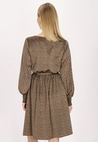 Rochie florală maro cu mâneci lungi și umflate, talie cinstită și fustă evazată. Fabricată dintr-un material neted cu un luciu subtil.