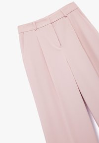 Helle rosa maßgeschneiderte Hose mit Falten, aus glattem Material. Verfügt über Seitentaschen und ein sauberes Design des Hosenbunds.