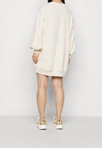 Kermanvärinen oversized-huppari-mekko, jossa on pitkät, ilmapallomaiset hihat ja ribbauskut. Vaatteena valkoiset ja beiget urheilukengät, joissa on oransseja yksityiskohtia.