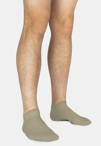 Beige Knöchelsocken mit einer glatten Textur, ausgestattet mit einem gerippten Bund und einem kleinen schwarzen Logo, das an der Seite aufgedruckt ist.