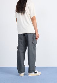 Beige bomullströja med korta ärmar, i kombination med grå cargobyxor med sidofickor och en avslappnad passform, bärs med vita sneakers.