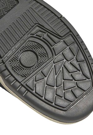 Suela de sandalia de goma negra con patrones geométricos y en zigzag, incluyendo una sección circular texturizada cerca del talón.