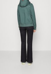 Teal, hooded jacket with a front zipper and elastic cuffs, paired with dark denim flared jeans and light sneakers. Simple design and texture.