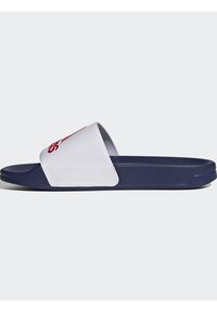 Sandalia tipo slip-on con una tira sintética blanca que muestra texto rojo, suela azul marino, diseño plano, parte superior texturizada y estilo minimalista.