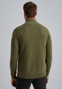 Olivengrüner strukturierter Pullover mit hohem Kragen, gerippten Bündchen und Saum. Mit einem Patches-Akzent auf der linken Schulter.