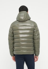Grøn polstret jakke med en blank finish, der har vandrette quiltede sektioner, hætte og elastiske manchetter. Bagudsigten viser en glat tekstur.