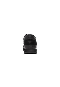 Zapatilla deportiva negra con parte superior de tela texturizada, puntera redondeada y suela plana, que presenta un sutil logo en el talón y acentos en contraste.