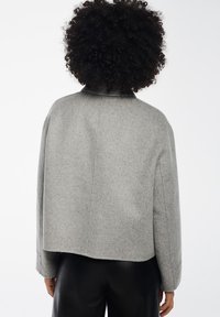 Szara kurtka o kroju cropped z mieszanki wełny, o gładkiej teksturze, wysokim kołnierzu i lekko opuszczonych ramionach, prezentująca minimalistyczny design.