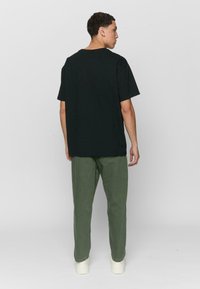 Black cotton t-shirt with a relaxed fit, short sleeves, and a round neckline, paired with olive green cotton pants and white sneakers.