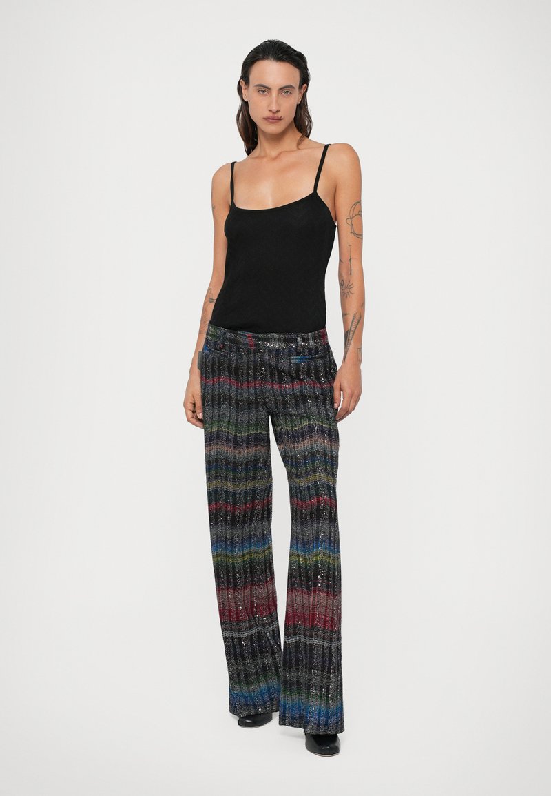 Débardeur noir à fines bretelles associé à un pantalon large taille haute multicolore, pailleté, avec des rayures verticales et des plis.