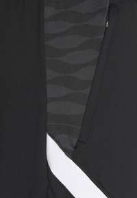 Gros plan sur un tissu noir avec un motif ondulé gris foncé texturé et un détail d’une bande blanche diagonale.