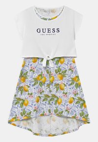 Valkoinen lyhythihainen paita, jossa on "GUESS LOS ANGELES" -logo, yhdistettynä kukalliseksi sitruunakuosiseksi hameeksi. Hameessa on solmittava yksityiskohta vyötäröllä.