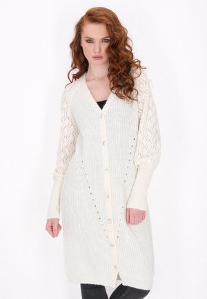 Cardigan lungo in crema a maglia, con una texture a coste, maniche a motivo pizzo e cinque bottoni frontali, caratterizzato da una silhouette rilassata.