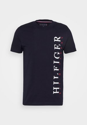 Mørkeblå kortærmet t-shirt med vertikal hvid "HILFIGER" tekst og små røde bogstaver på højre side.