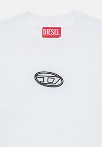 Balta kokvilnas T-kreklā ir sarkans "Diesel" uzlīmes un melns izšūts ovāls logo priekšpusē, demonstrējot mūsdienīgu minimālisma dizainu.