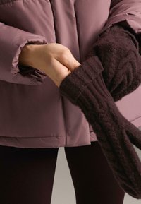 Jachetă matlasată mov, combinată cu mănuși tricotate maro închis, cu textură rigidă și model cu cablu.