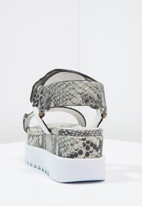 Klasické sandály s bílou platformou, šedými a černými popruhy se vzorem hadí kůže a nastavitelným kotníkovým páskem, pohled zezadu.