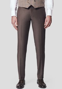Brązowe spodnie o dopasowanym kroju, wykonane z gładkiego materiału, z prostymi nogawkami, złożonymi plisami z przodu oraz subtelnym połyskiem, w połączeniu z brązowymi butami.