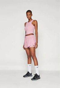 Light pink activewear set featuring a cropped tank top and matching shorts, paired with black athletic shoes and white knee-high socks.