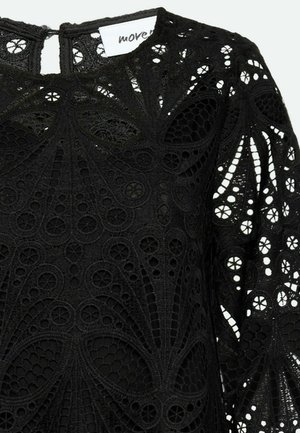 Čierny čipkový top s zložitými, vrstvenými vzormi a výrezmi, s dlhými rukávmi a uzáverom na zadnej strane v tvare kľúča.