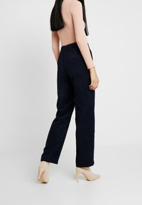 Mörkblå kordflosströjor med bred passform, texturerat tyg och elastisk midja, kombinerat med hudfärgade högklackade skor.