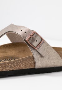 Sandál Birkenstock s metalickou šedou koženou svrchní částí, bronzovou sponou a texturovanou korkovou stélkou. Černá gumová podrážka.