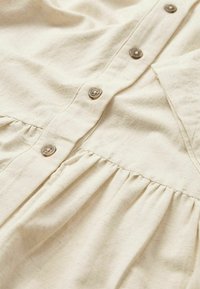 Abito in cotone color crema con bottini frontali, caratterizzato da una gonna arricciata e una texture liscia con dettagli di cucitura visibili.