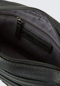Schwarze Lederhandtasche mit einem glatten Innenfutter, versehen mit einer Reißverschlusstasche und einem Stoffetikett. Dunkle Fütterung mit feiner Naht.
