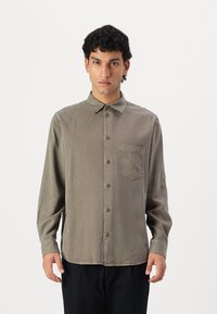 Khaki blouse met knopen, een kraag, lange mouwen en een patchzak aan de linkerkant. Zachte stof met een licht vervaagde textuur.