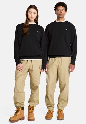 Felpe nere con un piccolo logo, pantaloni cargo beige e stivali marroni stringati. Vestibilità comoda con maniche lunghe e polsini elasticizzati.